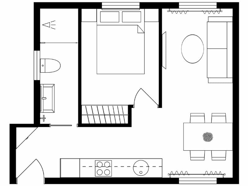 Black and white floor plan of a small apartment or studio layout. The design includes a bedroom with a double bed, a bathroom with a toilet, sink, and bathtub, and an open living area. The living space contains a sofa, round coffee table, dining table with four chairs, and a kitchen along one wall with a stove, sink, and countertop. The entrance is at the bottom left corner, and a staircase is positioned between the bedroom and living area. Furniture and fixtures are drawn with simple line art.