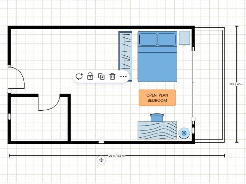 2D floor plan made with a template in Canva. The floor plan shows a two-room floor plan with a balcony and blue furniture such as a double bed, a closet, a nightstand, a desk with a chair and a lamp. There is also an orange label saying "open-plan bedroom". There are measurements showing the size of the floor plan outside the walls of the floor plan.