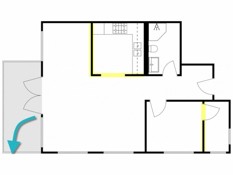 Simplified 2D floor plan of an apartment with key features highlighted in yellow, showing kitchen, bathroom, bedroom, living area, and balcony. A large blue arrow indicates the main entrance from the balcony. Yellow highlights mark structural walls or key design elements.