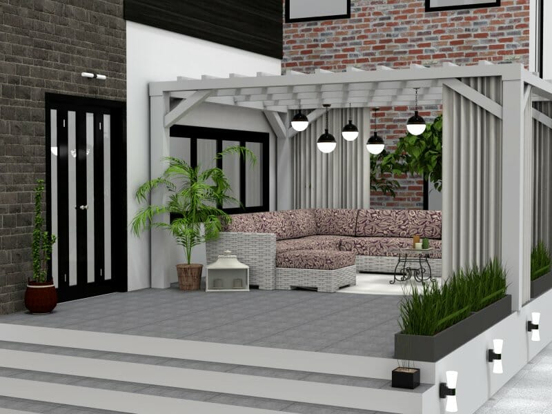 3D-rendered image of a modern outdoor patio with a pergola. The seating area features an L-shaped wicker sofa with patterned cushions, hanging pendant lights, potted plants, and decorative accents. The surrounding architecture includes a mix of brick and dark stone walls, black-trimmed windows and doors, and a wide tiled stairway leading up to the space.